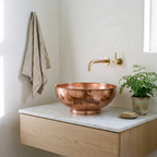 Copper bowl vessel sink on a floating white oak vanity in a bright powder room