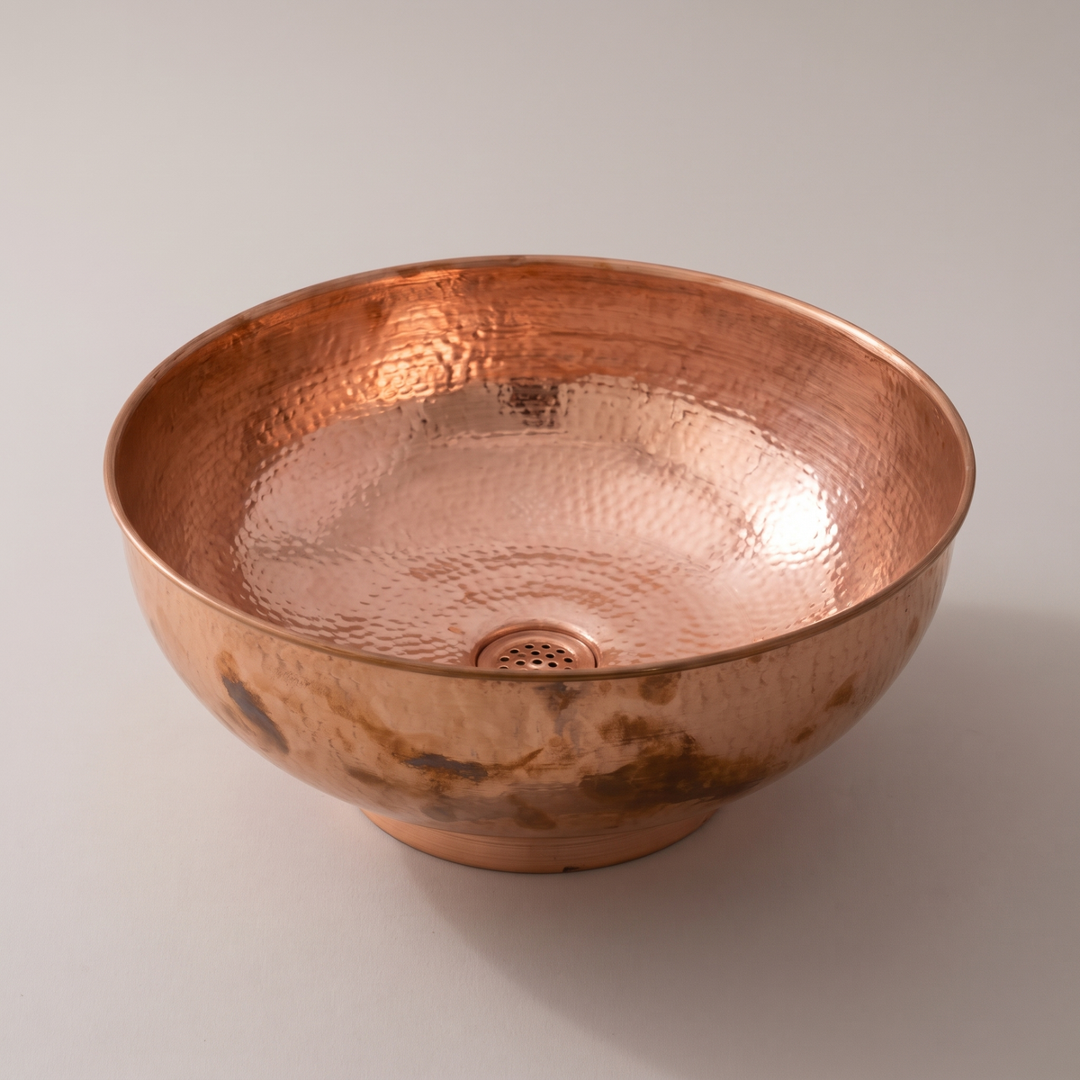 Round copper vessel bowl with rolled rim, foot ring and hammered interior on a plain background