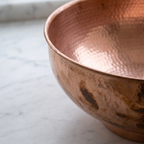 Close-up of the rolled rim, hammered copper interior and dark patina patches of a copper vessel sink