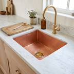 Square hammered copper undermount sink with brass basket strainer in a white marble kitchen counter