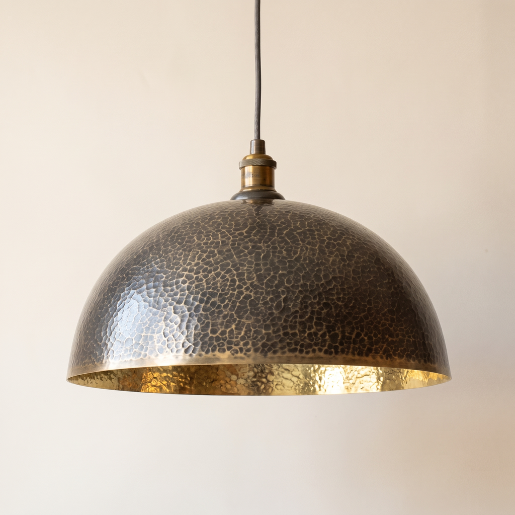 Hammered brass dome pendant with dark patina outside and bright brass inside on a light background