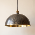Hammered brass dome pendant with dark patina outside and bright brass inside on a light background