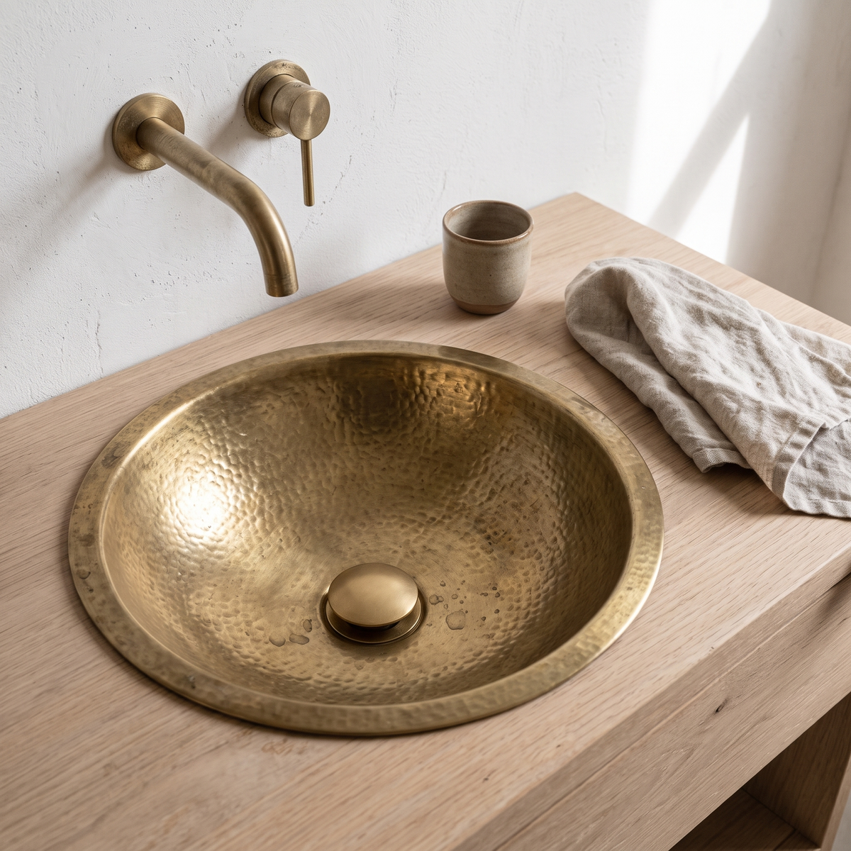 Unlacquered brass push-up drain in a hammered brass drop-in sink on a white oak vanity