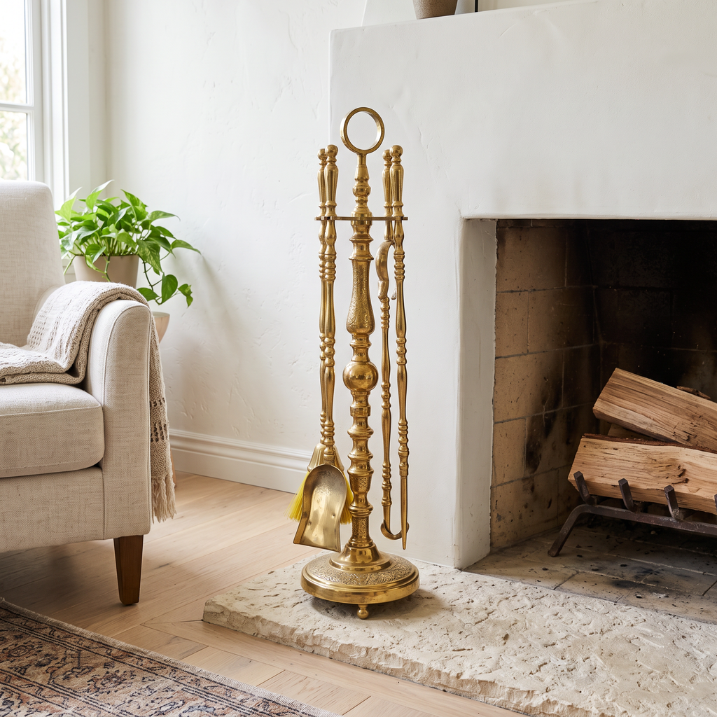 Unlacquered brass fireplace tool set with ring-top stand on a limestone hearth beside a white plaster fireplace