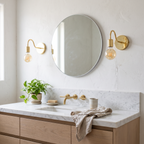 Pair of unlacquered brass gooseneck wall sconces beside a round bathroom mirror