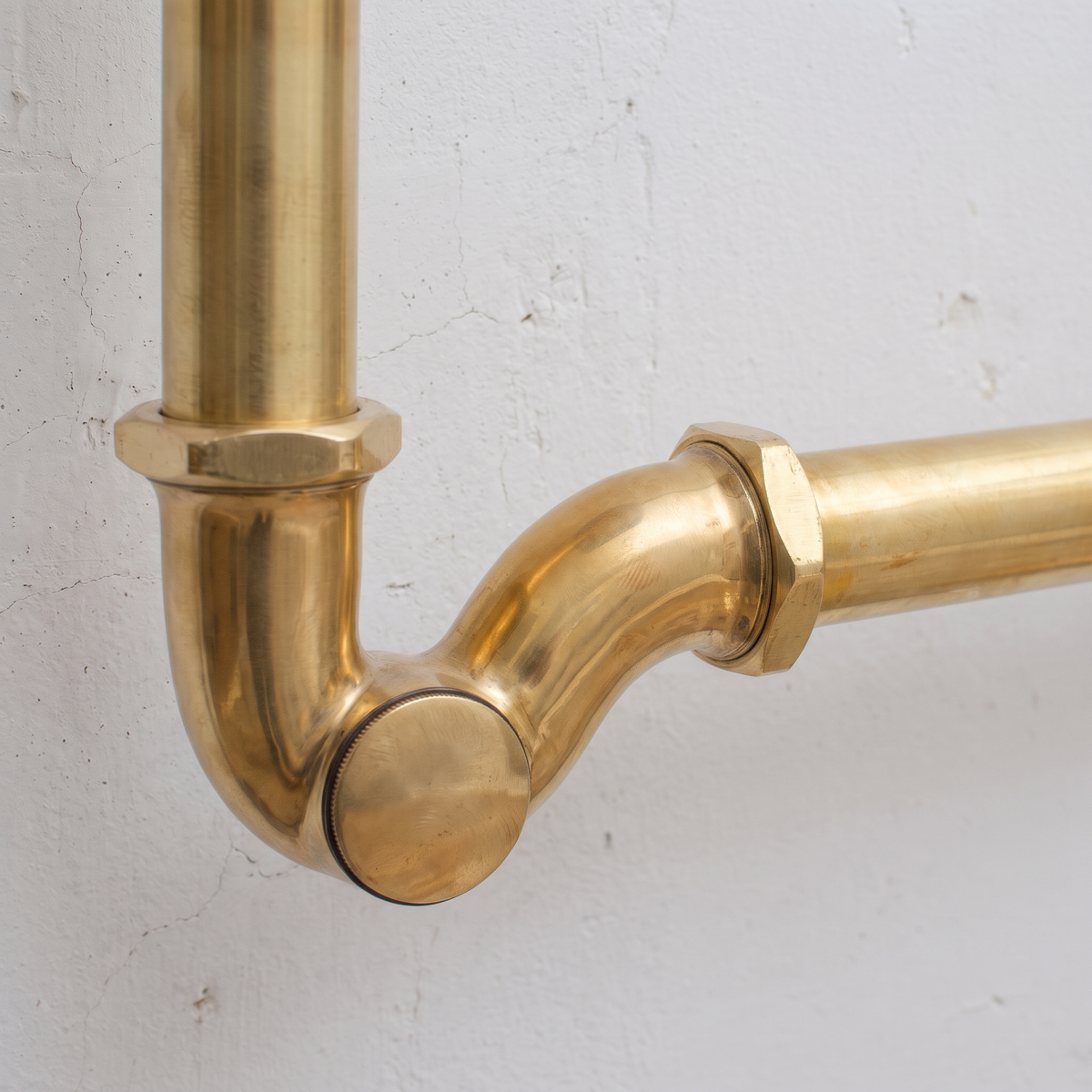 Close view of the brass J-bend and slip nut against a plaster wall