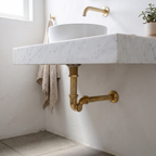 Unlacquered brass P-trap under a floating marble vanity in a bright bathroom