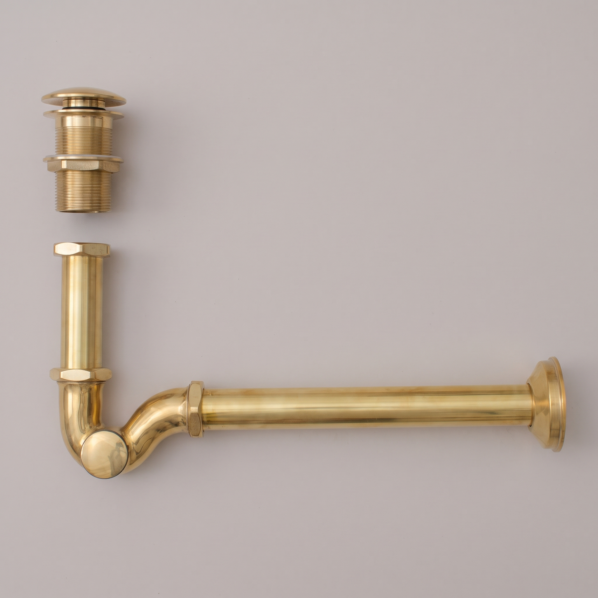 Unlacquered brass P-trap kit and push pop-up drain on a light background