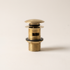 Unlacquered brass push-up drain with overflow slot and threaded body on a light background