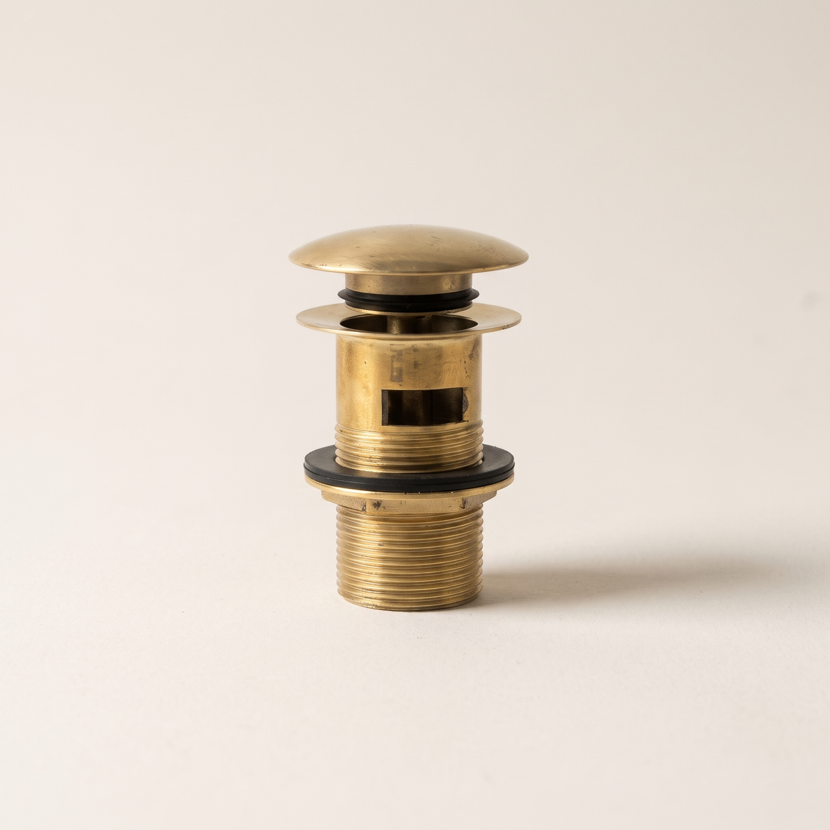 Unlacquered brass push-up drain with overflow slot and threaded body on a light background