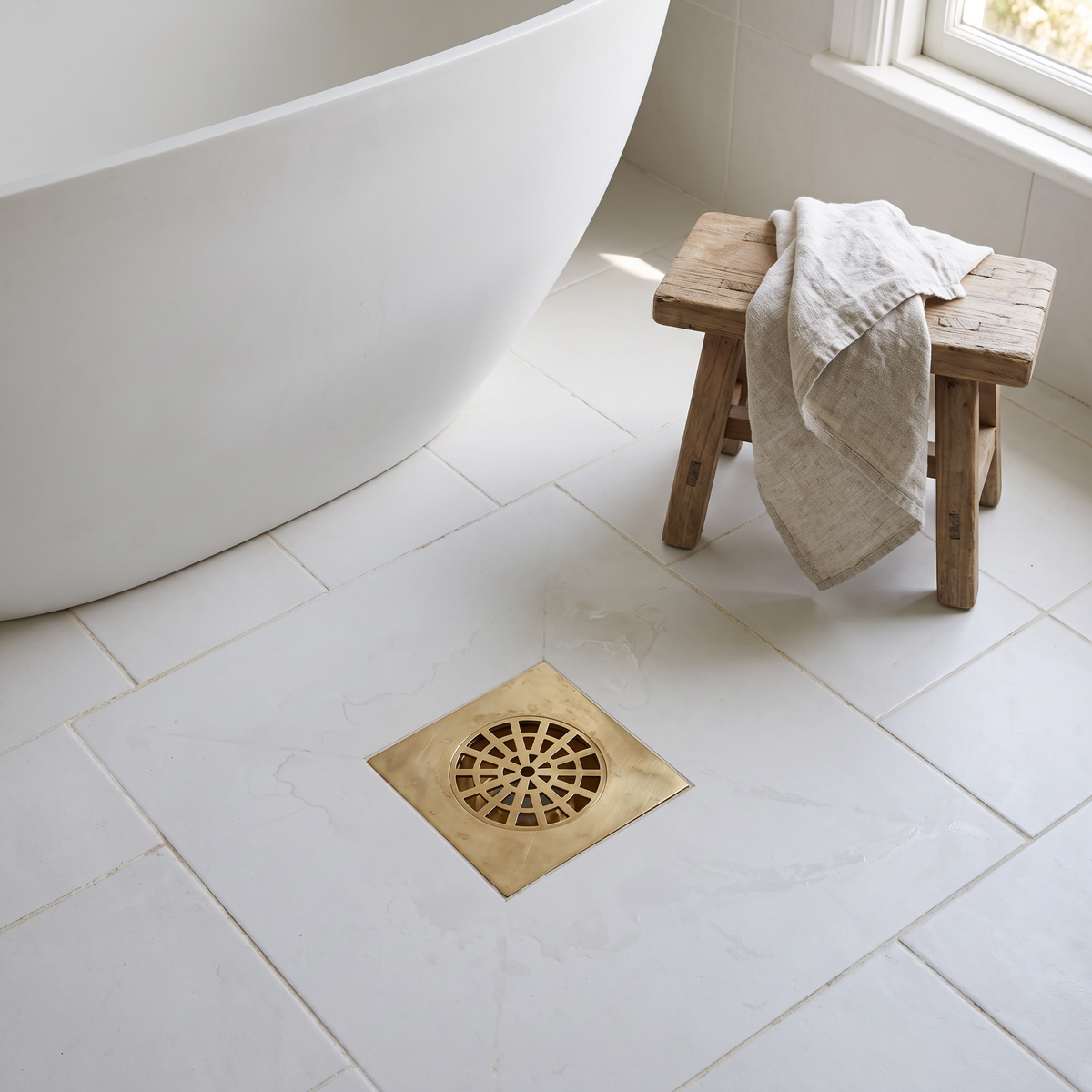 Brass shower drain with round grate in a white tiled wet room