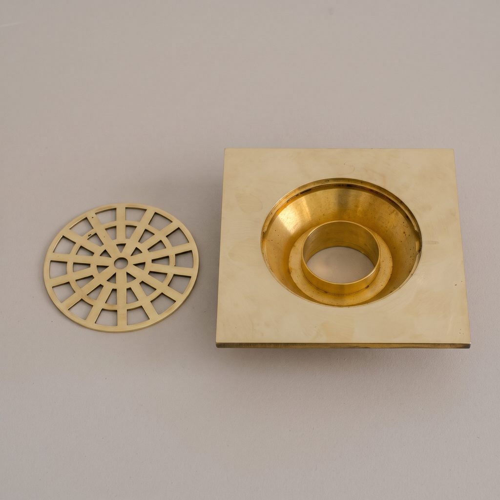 Unlacquered brass square shower drain with round web grate on a light background