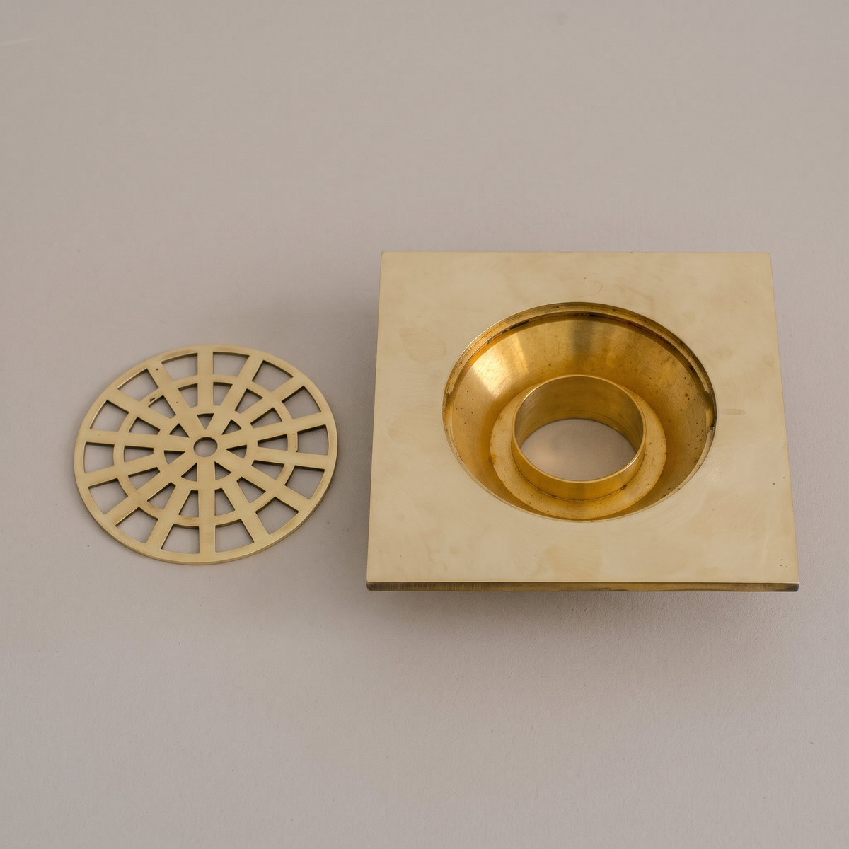 Unlacquered brass square shower drain with round web grate on a light background