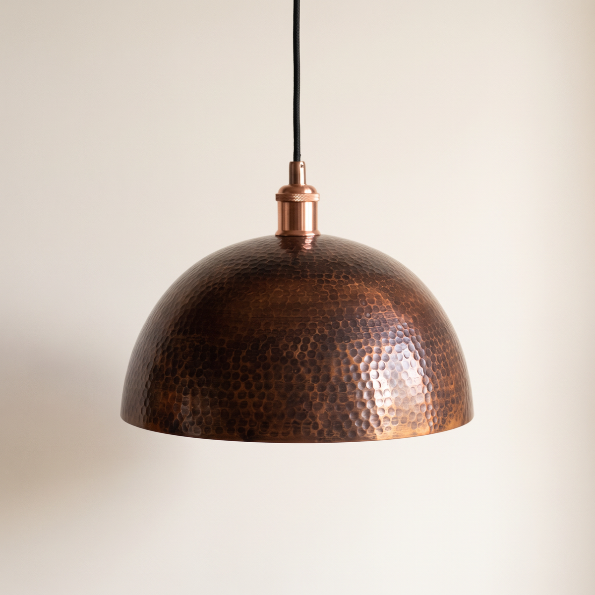 Dark oxidized hammered copper dome pendant with black cord on a light background
