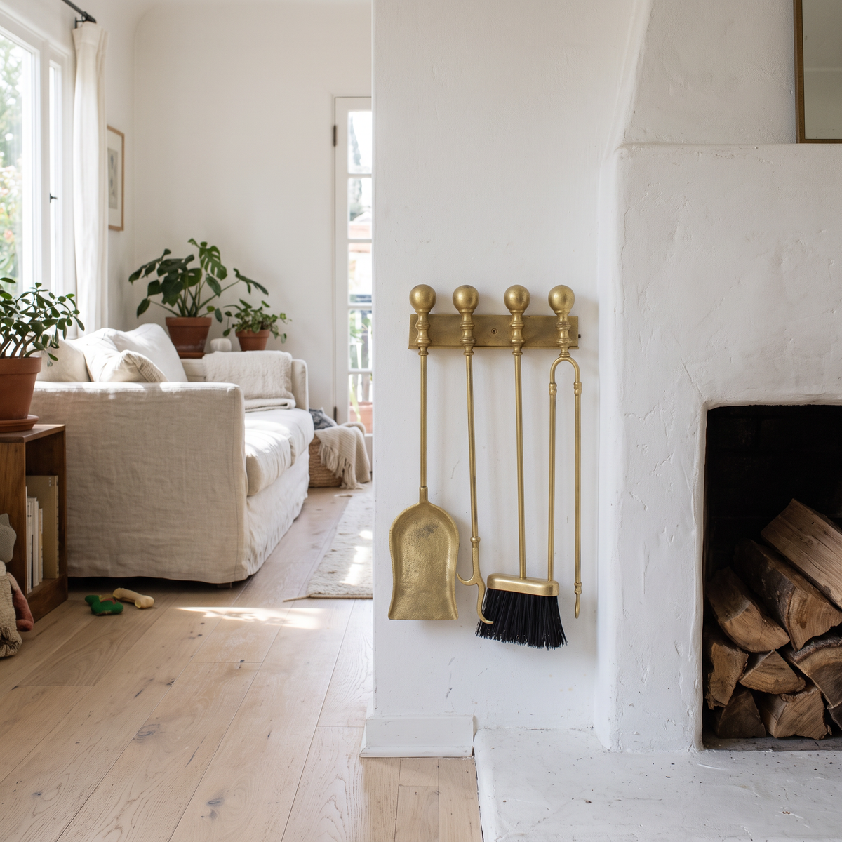 Aged brass fireplace tools on a ball-finial wall rack beside a white plaster fireplace