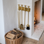 Polished brass fireplace tools hung beside a limestone fireplace with a basket of logs