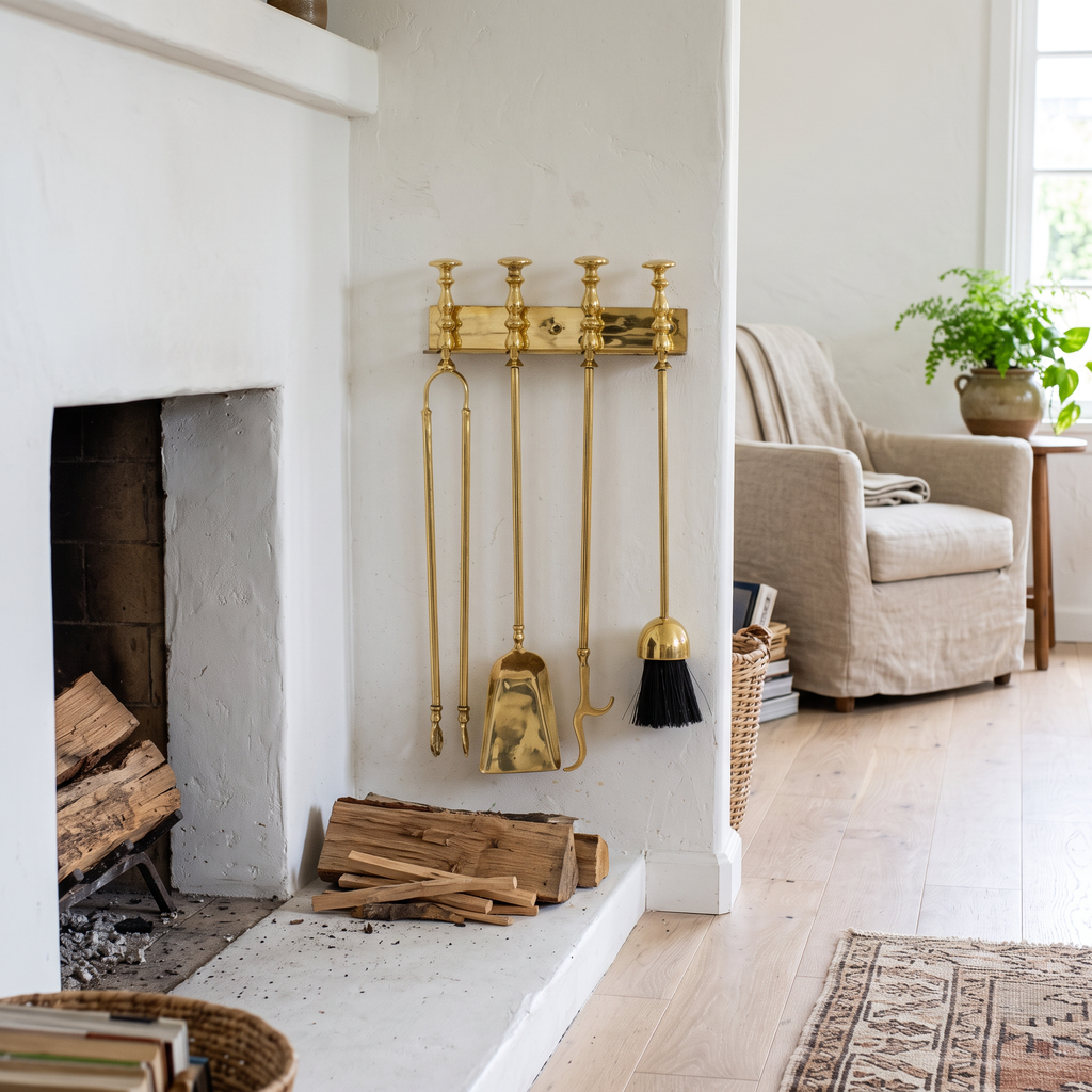 Wall-mounted polished brass fireplace tools beside a white plaster fireplace in a living room