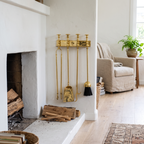Wall-mounted polished brass fireplace tools beside a white plaster fireplace in a living room